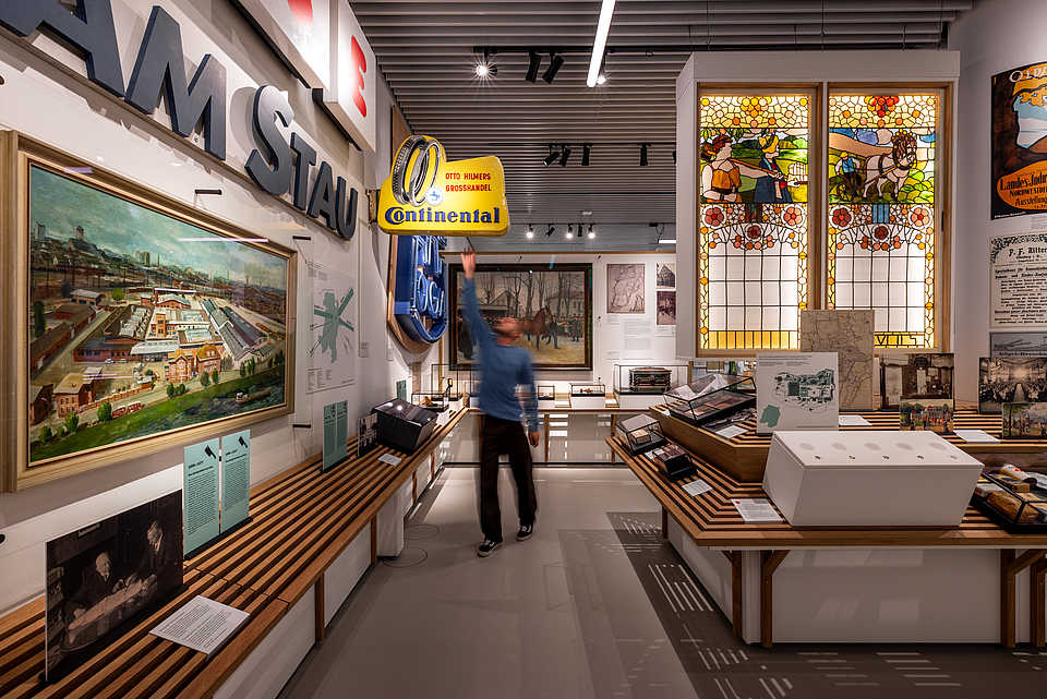 Ausstellungsbereich zur Oldenburger Stadtgeschichte mit historischen Werbeschildern, Gemälden und farbigen Glasfenstern.