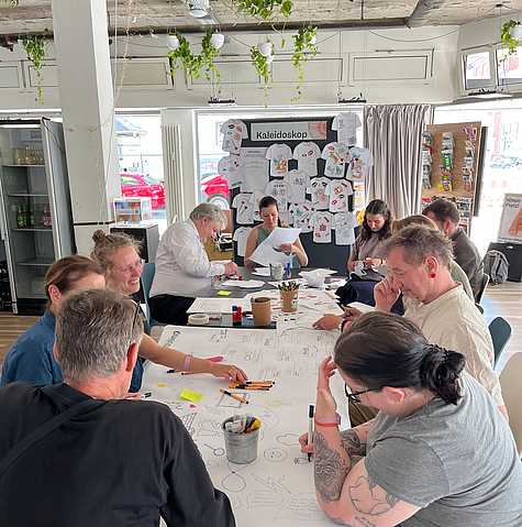 Workshopgruppe arbeitet gemeinsam an einem großen Tisch mit Notizen, Materialien und Skizzen für das neue Corporate Design.