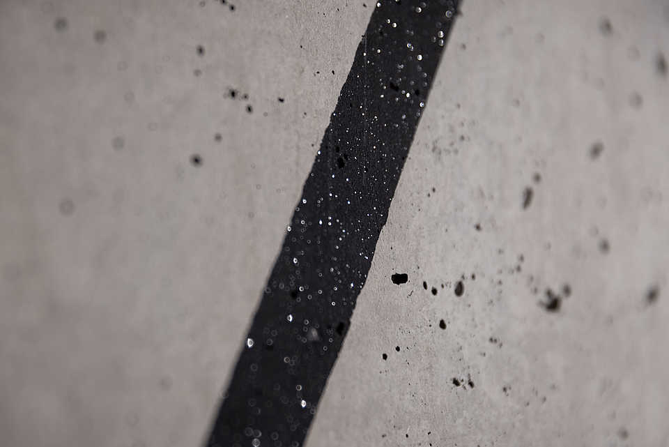 Eine Nahaufnahme einer schwarzen, schimmernden Linie, die über eine Betonwand verläuft.