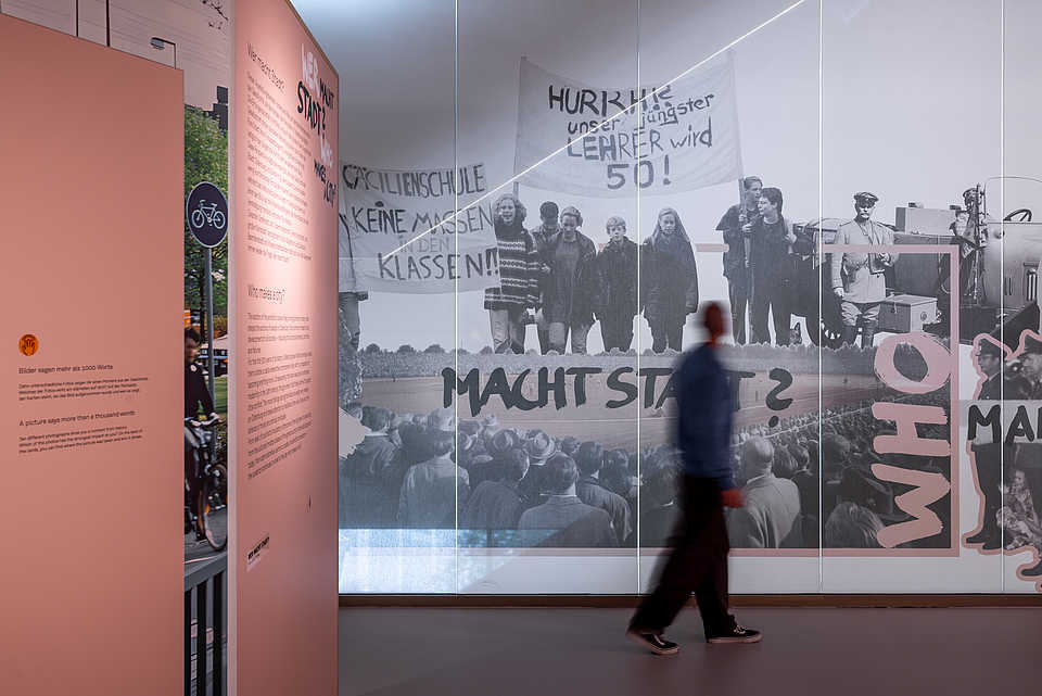 Besucher vor einer großformatigen Wandcollage mit historischen Protestfotografien und dem Schriftzug ‚Wer macht Stadt?‘.