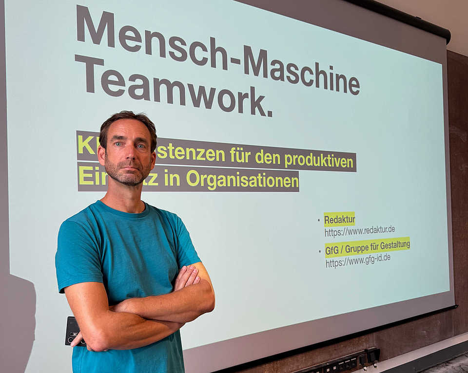 Person steht vor einer Präsentationsfolie mit dem Titel ‚Mensch-Maschine Teamworkz. KI-Assistenzsystemen in Organisationen‘
