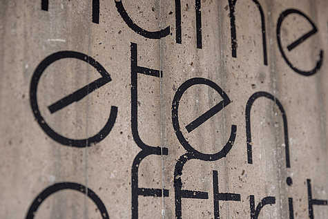 Ein detailreiches Foto einer Betonwand mit schwarzer Schrift. Der Text 'kamern, eten, afftritt' ist klar zu erkennen, mit einem Pfeil, der den Weg weist.