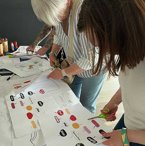 Zwei Workshopteilnehmerinnen gestalten gemeinsam eine Collage mit Symbolen, Farben und Gestaltungselementen.