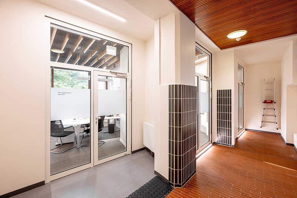 Eingangsbereich mit Säule und Fliesen im Aalto-Stil, kombiniert mit modernen Glastüren.
