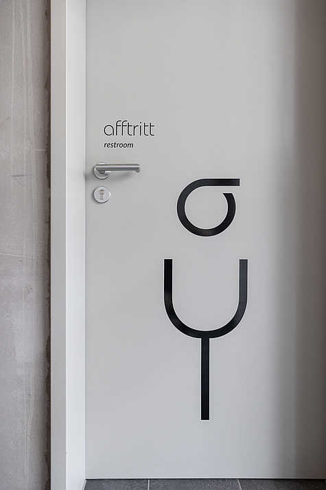 Weiße Toilettentür mit dem Schriftzug 'afftritt' und darunter 'restroom', gestaltet in einer modernen, kreativen Typografie.