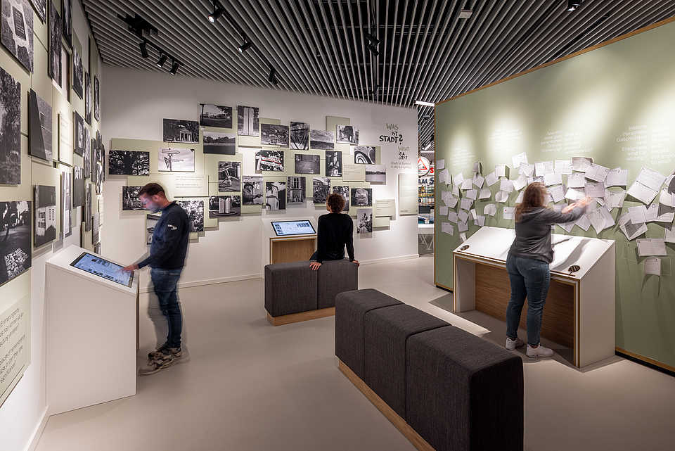 Besucher:innen an interaktiven Stationen und einer mit zahlreichen Beiträgen gestalteten Wand in der Dauerausstellung.“