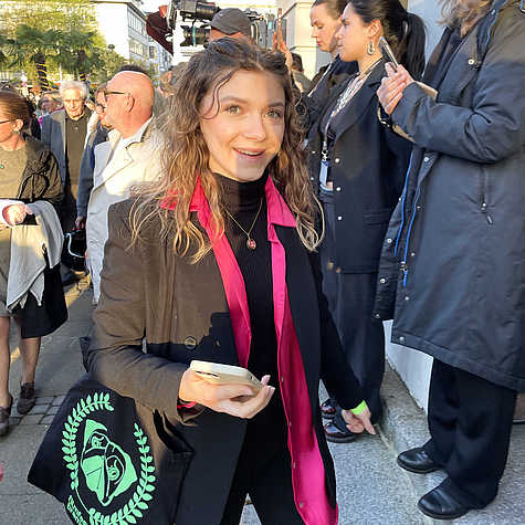 Alea lächelnd vor dem roten Teppich. Auf ihrer Tasche ist das grüne Logo des Filmfest Bremen zu sehen.