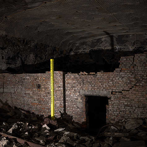 Mauer im Stollen der KZ-Gedenkstätte Mittelbau-Dora, mit Geröll auf dem Boden und gelber Markierung: ‚Office for Civilian Workers‘.