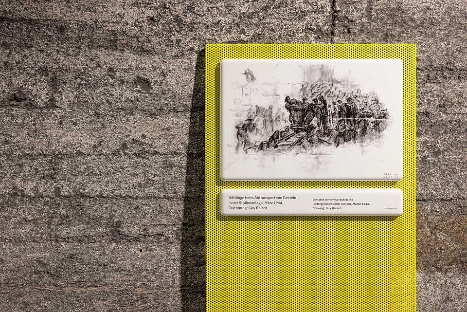 Ausstellungstafel mit einer Zeichnung von Guy Boisot aus dem Jahr 1944. Die Darstellung zeigt Häftlinge beim Abtransport von Gestein im unterirdischen Stollen Mittelbau-Dora.