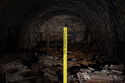 Blick in eine Tunnelkammer der Gedenkstätte Mittelbau-Dora mit Trümmern auf dem Boden. Im Vordergrund gelbe Markierung ‚Chamber 46‘.