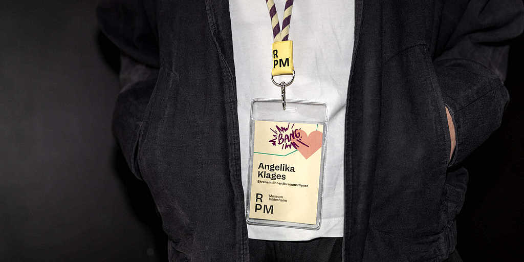 Mitarbeitende des RPM Museums Hildesheim tragen einen Namensausweis im neuen Corporate Design mit farbenfroher Gestaltung und Museumsschlüsselband.