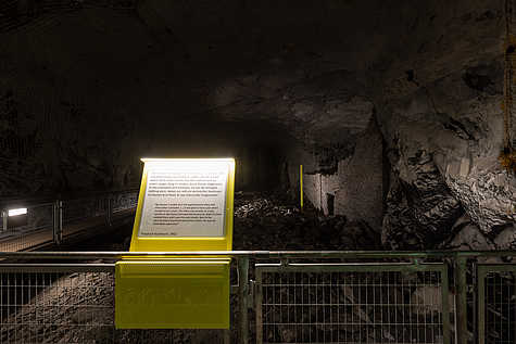 Ausstellungstafel mit Zeitzeugenbericht von Friedrich Kochheim aus dem Jahr 1952 in einem Stollenabschnitt der Gedenkstätte Mittelbau-Dora. Im Hintergrund eine zerstörte Mauer.“