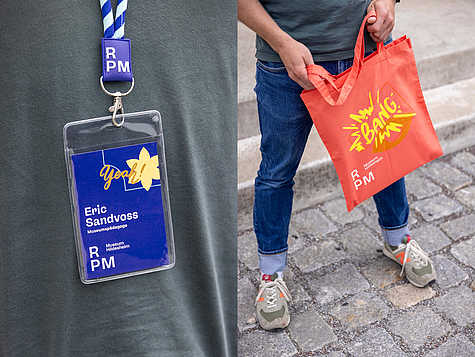 Badge und farbig gestaltete Stofftasche im Corporate Design des RPM Museums.