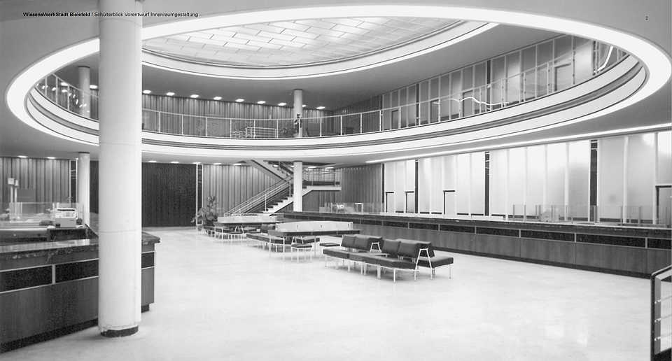 Innenansicht des ehemaligen Hauptsitzes der Sparkasse Bielefeld, ein modernes Gebäude mit geschwungener Architektur, großen Fensterflächen und zentraler Treppe in einem offenen Raum.