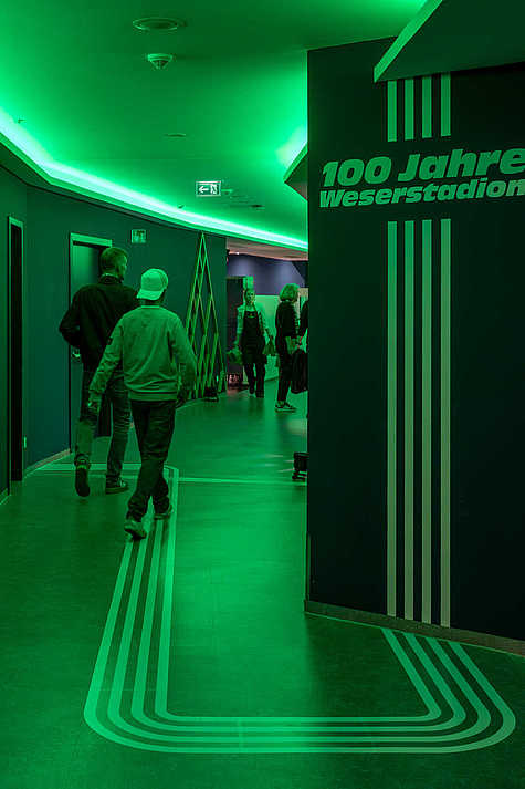 Grafische Linienführung zu 100 Jahre Weserstadion in einem grün beleuchteten Stadionflur
