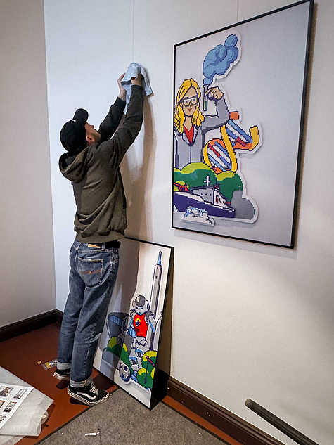 Einblick in den Aufbau der Ausstellung 'GfG Zeigen' mit Personen, die Kunstwerke positionieren und den Ausstellungsraum vorbereiten. Im Vordergrund sind Gemälde und andere kreative Werke sichtbar.