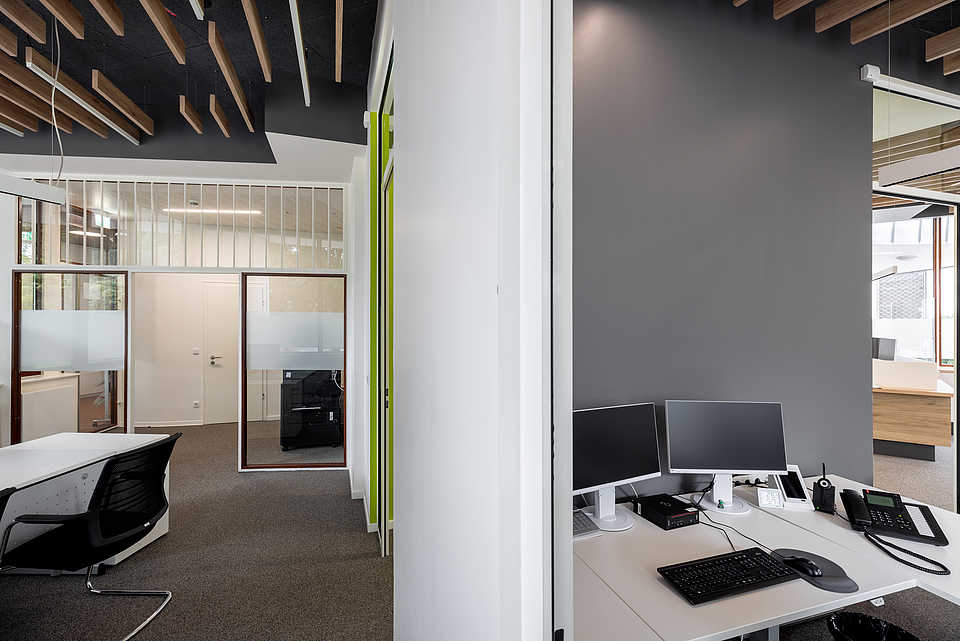 Bürobereich mit Sicht ins Großraumbüro, Glaswände mit Milchglasstreifen und schwarzer Rasterdecke.