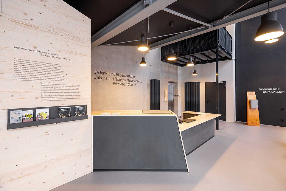 Empfangsbereich mit Holzwand, Informationsschriften, Schriften an der Wand und einer Rezeption.