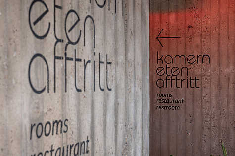 Die Aufschrift "kamern eten afftritt" ist auf Sichtbeton geschrieben. Die Schrift ist modern und minimalistisch.