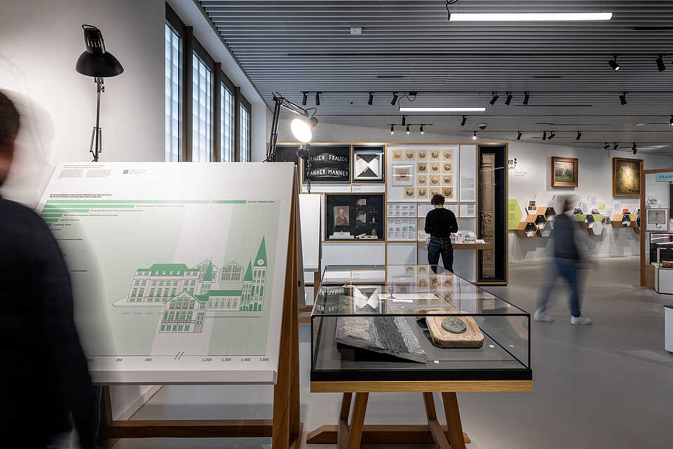 Blick durch die Dauerausstellung mit historischen Exponaten, Grafiken und Besucher:innen.