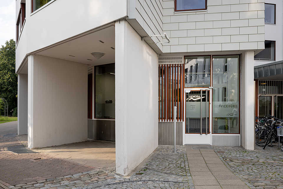 Außenaufnahme des Eingangsbereichs zum GEWOBA-Servicebüro mit Flachdach, weißen Fassadenelementen und Glasfront.