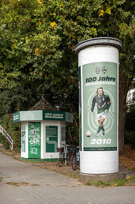 Gestaltung zu 100 Jahre Weserstadion auf einer Litfaßsäule und einem Kiosk vor dem Stadion