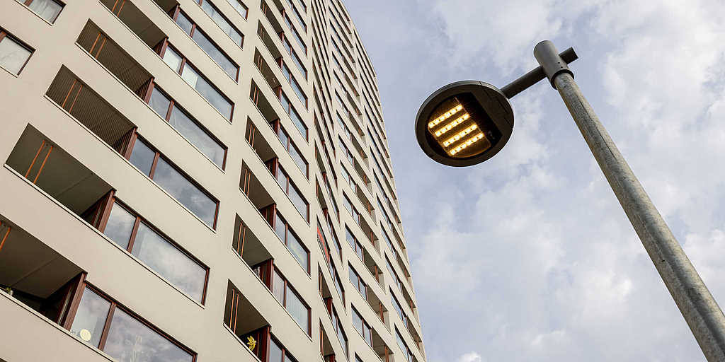 Blick nach oben auf die Fassade des Aalto-Hochhauses, daneben eine moderne Straßenlaterne vor bewölktem Himmel.