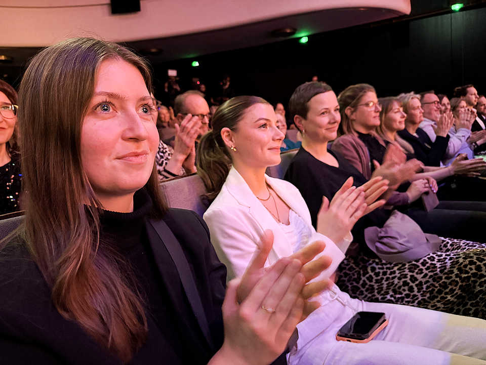 Publikum applaudiert während der Gala beim Filmfest Bremen 2025. Im Vordergrund sitzen Alea und zwei Kolleginnen, begeistert von der Bühnenshow.